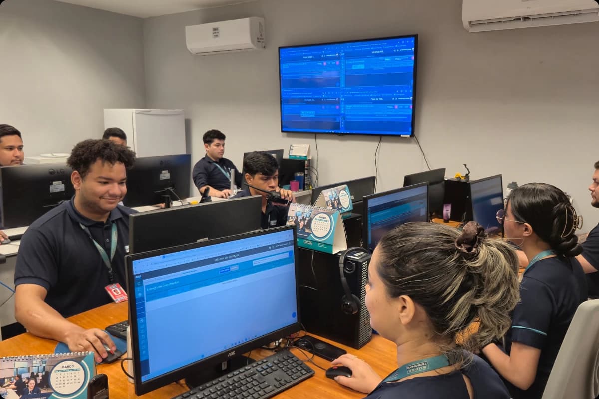Sala da ti do SuperTerminais com pessoas trabalhando em computadores e telas exibindo dados logísticos