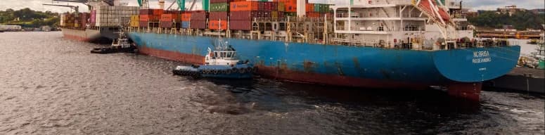 Operação portuária com navio e barcaças em área fluvial, representando logística com foco ambiental