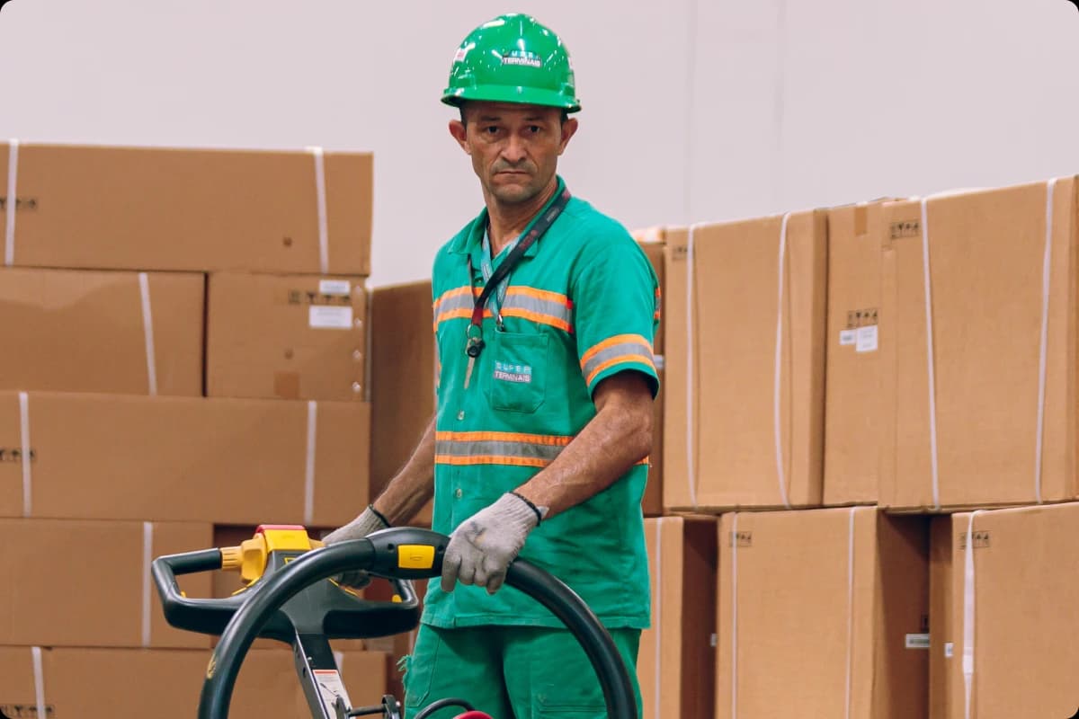 Trabalhador conduzindo uma empilhadeira no terminal portuário, usando equipamentos de segurança e uniforme de trabalho